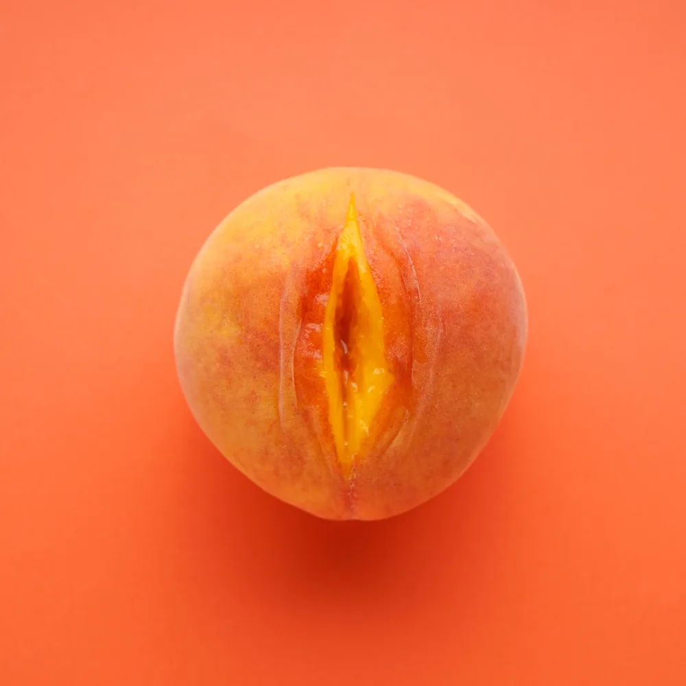 Melocotón maduro abierto sobre fondo naranja, imagen conceptual que simboliza la sensualidad femenina. Representación visual creativa para la categoría de juguetes para ellas en Karmasex.es