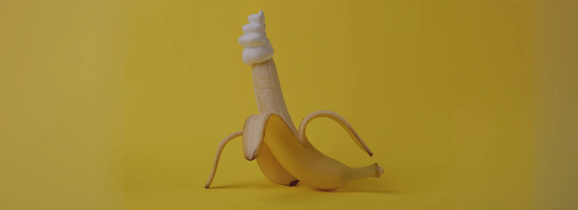 Plátano parcialmente pelado con nata en la punta sobre fondo amarillo, metáfora visual para juguetes para ellos.
