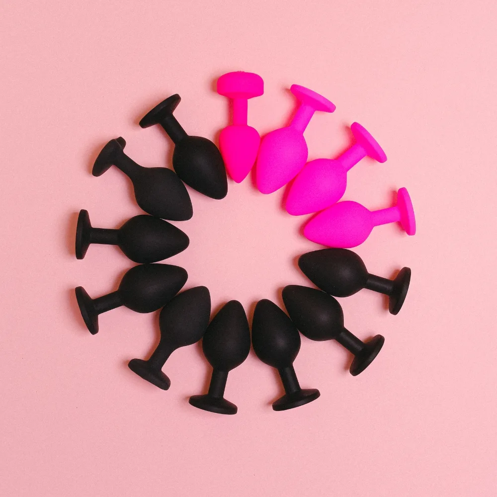 Juguetes anales de silicona en tonos rosa y negro dispuestos en círculo sobre fondo rosa, imagen para categoría de anal en Karmasex.es